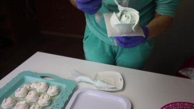 Hamur torbası ve başlık kullanan bir kadın gül şeklinde bir şekerleme oluşturur. Yaprakları yapıyor. Tepsinin üzerinde dengelemek için bir lokum var.