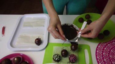 Bir kadın çikolata süngeri topunu yüzeye serer. Süslerle süslenmiş. Patates keki yapıyor. Tabakların yanında kek kurusıkı, sıvı çikolata ve renkli serpinti var..