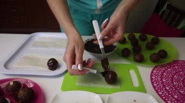 Bir kadın çikolatalı kek toplarının üzerine uzanır. Parıldıyor. Patates keki yapıyor. Tabakların yanında kek kurusıkı, sıvı çikolata ve renkli serpinti var..
