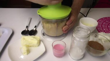 Bir adam blender kasesinde kurabiye kırar. Öğütme derecesini kontrol eder ve işleme devam eder. Patates kurabiyesi yapımında kullanılan diğer malzemeler de yakınlarda..