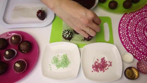 一个女人用撒满巧克力球装饰.做一个土豆蛋糕。盘子旁边是蛋糕、液体巧克力和彩色洒水. — 图库视频影像