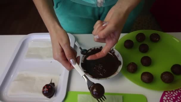 Žena položí na povrch čokoládovou houbovou kouli. Dělá bramborový dort. Vedle talířů jsou dortové polotovary, tekutá čokoláda a barevné posypy. — Stock video