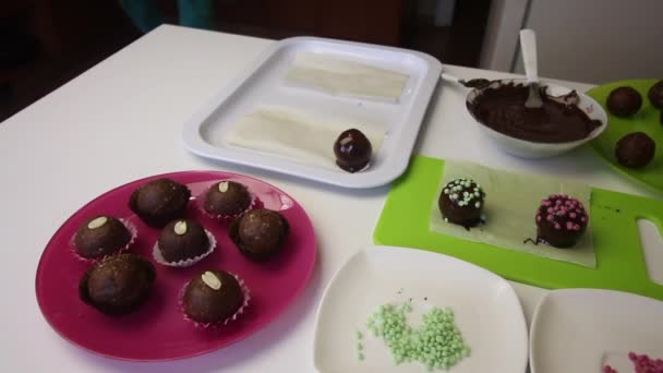 一个女人把巧克力球撒在海绵蛋糕上.做一个土豆蛋糕。盘子旁边是蛋糕、液体巧克力和彩色洒水.. — 图库视频影像