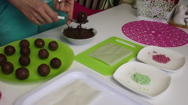 Uma mulher mergulha bolas de bolo de esponja em chocolate. Faz um bolo de batata. Ao lado das placas estão bolos em branco, chocolate líquido e polvilhas coloridas — Vídeo de Stock