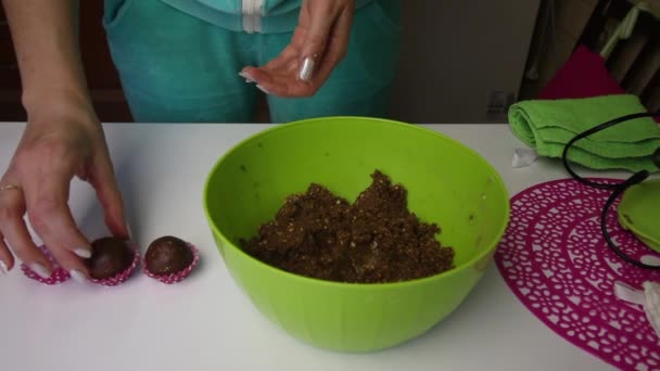 Una mujer pone una bola de pulpa de galleta en papel. toma de corriente. Luego toma la masa del recipiente y rueda bolas nuevas con las manos. La masa es marrón, hecha de migas de galletas y cacao, con — Vídeo de stock