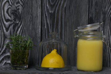 Cam kavanozda limonlu kurabiye. Yakınlarda cam kapaklı bir konteynırda yarım limon var. Bardakta bir demet biberiye. Fırçalanmış tahtaların arka planına karşı.