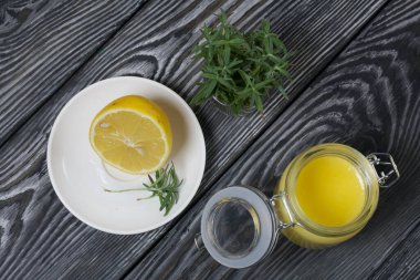 Cam kavanozda limonlu kurabiye. Yakınlarda bir tabakta yarım limon ve biberiye var. Fırçalanmış tahtaların arka planına karşı.