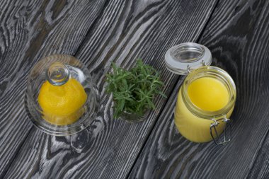 Cam kavanozda limonlu kurabiye. Yakınlarda cam kapaklı bir konteynırda yarım limon var. Bardakta bir demet biberiye. Fırçalanmış tahtaların arka planına karşı.