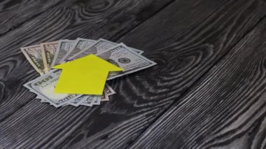 Masanın üzerinde dolar hayranı var. Üzerlerinde evin silueti yatar, kağıttan kesilmiş. Adamın biri üzerine bir sürü anahtar koymuş. Tahtalar üzerinde,.