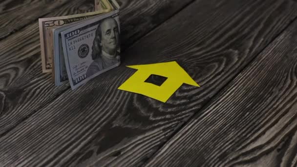 Op een tafel van geborstelde planken liggen dollarbiljetten. Vlakbij is het silhouet van een uit papier gesneden huis. Een man doet een hoop sleutels om hem heen.. — Stockvideo