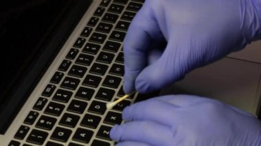 Lastik eldivenli bir adam laptopunu temizliyor. Bir pamuk çubuğu anahtarları temizler. Sonra dizüstü bilgisayarın klavyesini özel bir peçeteyle siliyor. Çalışan ekipmanların viral enfeksiyondan korunması.