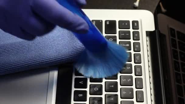 Een man met rubberen handschoenen maakt zijn laptop schoon. Een speciale borstel verwijdert stof van het toetsenbord en het laptopscherm. Bescherming van arbeidsmiddelen tegen een virusinfectie. — Stockvideo