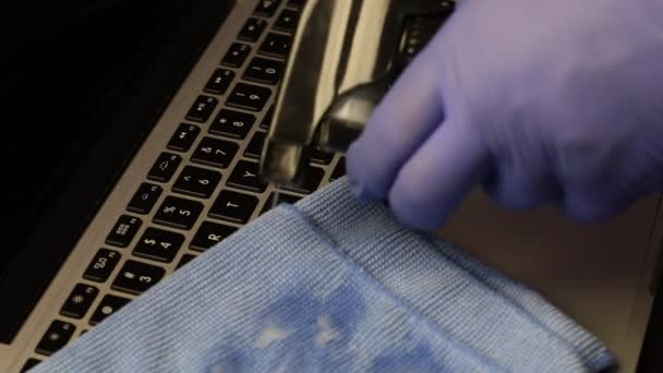 Um homem de luvas de borracha está a limpar o portátil. Aplica o detergente de uma garrafa de borrifo a um tecido e esfrega o teclado de computador portátil. Protecção do equipamento de trabalho contra uma infecção viral . — Vídeo de Stock