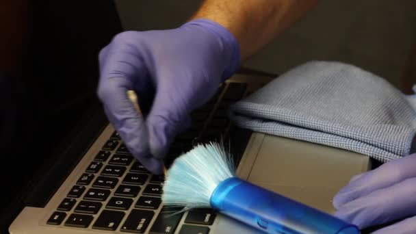 Чоловік в гумових рукавичках очищає клавіатуру ноутбука між ключами ватним тампоном. Прибирання та обслуговування ноутбука. Захист робочого обладнання від вірусних інфекцій — стокове відео