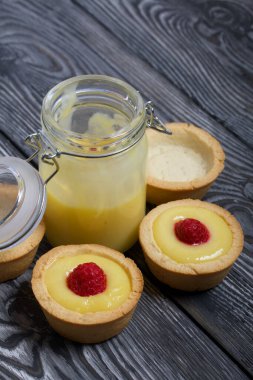 Limonlu turta. Ahududu ile süslenmiş. Siyah çam ağaçlarının üzerinde yatıyorlar. İçinde Kürt limonu olan açık bir kavanoz var. Yanlarında malzemesiz turtalar var..