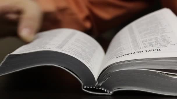 Sur la table se trouve une Bible ouverte. L'homme tourne rapidement les pages à la recherche du chapitre désiré. Trouve et positionne positivement un doigt au bon endroit. Gros plan .