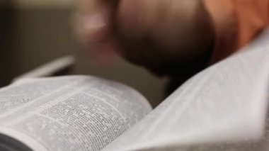 Masanın üzerinde açık bir İncil yatıyor. Doğru yeri bulmak için sayfaları yavaşça karıştıran bir adam. Yakın çekim..