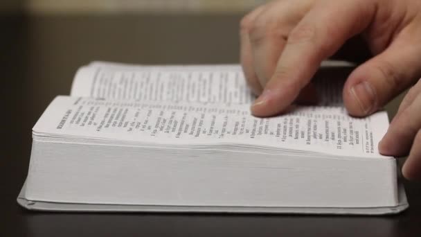 Sur la table se trouve une Bible ouverte. Un homme feuilletant lentement les pages à la recherche du chapitre désiré. Réorganise un signet. Gros plan . — Video