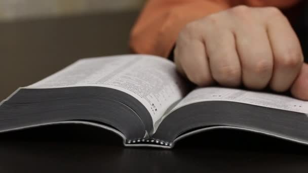 Sur la table se trouve une Bible ouverte. Un homme le lit, bouge son doigt le long des lignes, tourne les pages. Corrige un signet et ferme le livre. Gros plan 