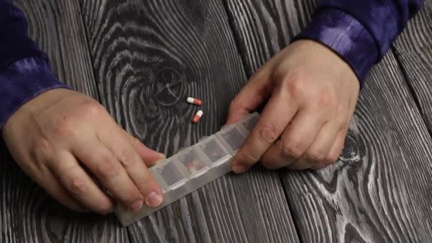 Ein Mann legt mehrere Tabletten in eine Tablettenbox und legt sie auf einen Tisch mit schwarzen gebürsteten Brettern. — Stockvideo