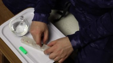 Bir adam ilaç kutusundan bir avuç hap ve bir bardak su alır. Önünde bir tablet ve cıva termometre var..