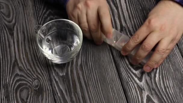 Een man neemt een pil uit een pil doos met pillen. Hij neemt een glas water in zijn andere hand. Tegen de achtergrond van een tafel van zwarte borstelplanken. — Stockvideo