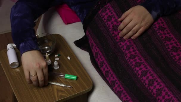 病人躺在铺有毯子的床上.用喷雾器喷喉咙.椅子旁边是各种药物. — 图库视频影像
