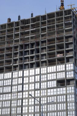 Yüksek binalar yapım aşamasında. Güçlendirilmiş beton çerçeve. Çift camlı pencerelerin kurulumu başlatılıyor. Görünür vinçler.