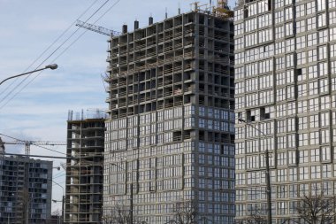 Yüksek binalar yapım aşamasında. Güçlendirilmiş beton çerçeve. Çift camlı pencerelerin kurulumu başlatılıyor. Görünür vinçler.