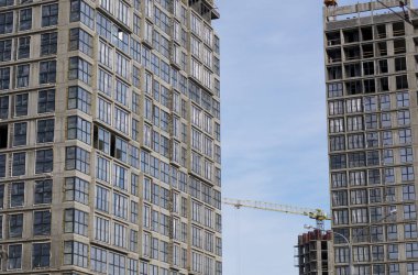 Yüksek binalar yapım aşamasında. Güçlendirilmiş beton çerçeve. Çift camlı pencerelerin kurulumu başlatılıyor. Görünür vinçler.