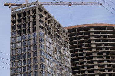 Yüksek binalar yapım aşamasında. Güçlendirilmiş beton çerçeve. Çift camlı pencerelerin kurulumu başlatılıyor. Görünür vinçler.