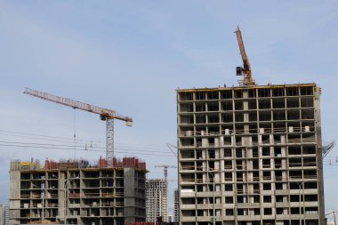 Yüksek binalar yapım aşamasında. Güçlendirilmiş beton çerçeve. Çift camlı pencerelerin kurulumu başlatılıyor. Görünür vinçler.