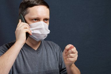 Tıbbi maskeli bir adam akıllı telefondan konuşuyor. Sohbet sırasında incir gösteriyor. Koronavirüs sırasında kendini izole eden enfeksiyonlara karşı koruma.