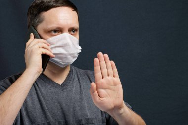Tıbbi maskeli bir adam akıllı telefondan konuşuyor. Sohbet sırasında avucuyla olumsuz bir hareket yapıyor. Koronavirüs sırasında kendini izole eden enfeksiyonlara karşı koruma.
