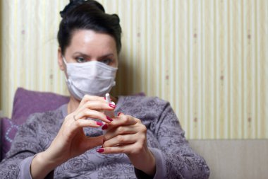 Tıbbi maskeli bir kadın yatağa oturur ve elinde bir burun spreyi tutar. Koronavirüs sırasında kendini izole eden enfeksiyonlara karşı koruma.