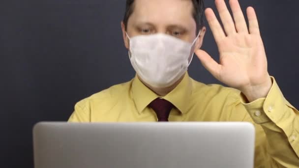 Seorang pria bertopeng medis membuka laptop dan berpartisipasi dalam komunikasi melalui internet. Gestur secara luas dan menunjukkan interlocutor semprotan tenggorokan. Mengisolasi diri sendiri selama epidemi coronavirus . — Stok Video