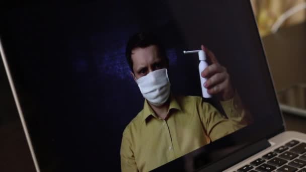 A video blogger in a medical mask is recording an advertising video on a laptop���s webcam. He presents to his subscribers a throat spray. For the prevention and treatment of viral infections during a — Stock Video