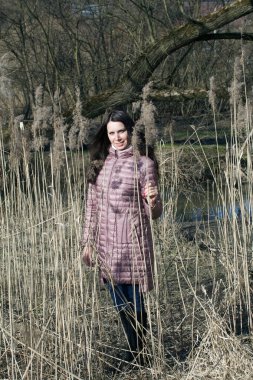 Bir kız bahar parkında yürüyor. Uzun ve kuru otların arasında duruyor..