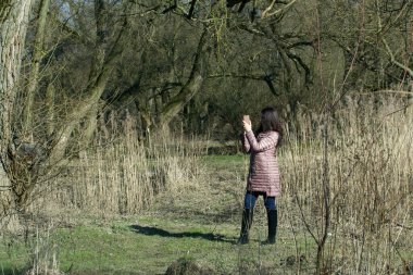 Bir kız bahar parkında yürüyor. Akıllı bir telefonun elindeydi. Doğanın bir fotoğrafını çeker..