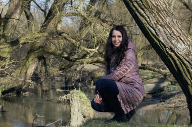 Bahar parkındaki kız. Nehir kıyısında çömeliyor.