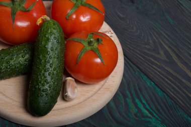 Salatalık, domates ve sarımsak. Yeşil at kuyruklu domatesler. Kesme tahtası fırçalanmış çam ağaçlarının yüzeyinde yatıyor..