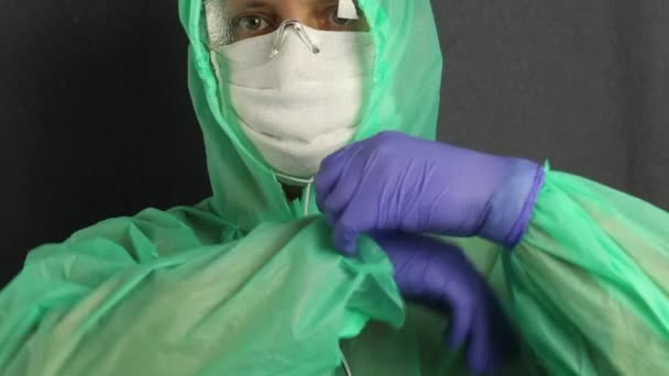 A man in a protective coat with a hood, a gauze mask and glasses on his face. He puts a rubber glove on his right hand and tucks a raincoat sleeve into it. Virus protection. — Stock Video