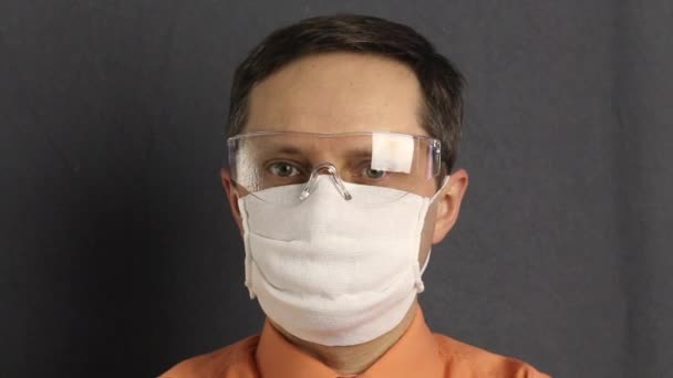 Un homme avec un masque de gaze. Il met des lunettes de sécurité, puis un manteau de protection. Redresse le capot avec ses mains. Protection contre les virus . — Video