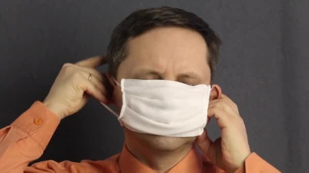 En man sätter på sig en gasbinda ansikte mask. Den klamrar sig fast vid hennes öron. Rak i händerna. Skydd av virus. — Stockvideo