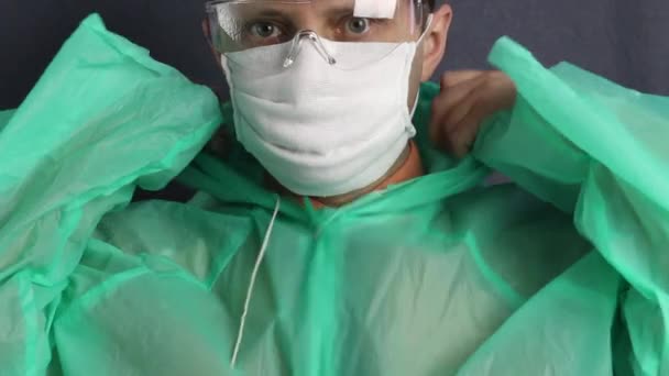 Un hombre con una capa protectora, máscara de gasa y gafas en la cara. Se pone una capucha y la ata. Protección contra virus . — Vídeo de stock