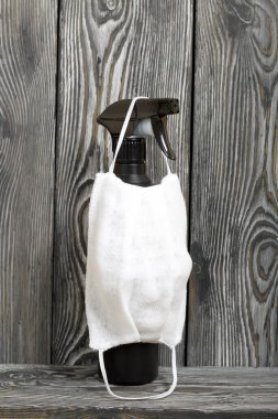 Dezenfektan spreyi ve gazlı bez yüz kalkanı. Virüs salgını sırasında kendini izole etmenin ve karantina altına almanın bir sembolü. Fırçalanmış çam ağaçlarının arka planında.