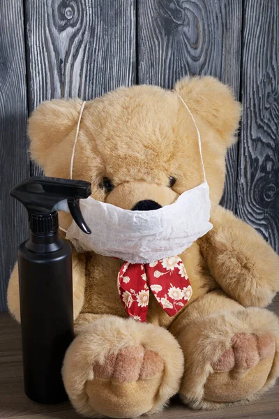 Soft toy, bear, in a protective gauze mask. In hand a spray bottle with a disinfectant. Against the background of brushed boards. Protection against a viral epidemic.
