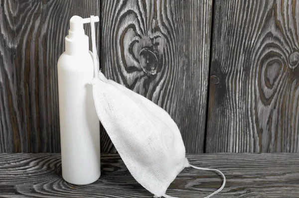 Disinfectant spray and gauze face shield. A symbol of global self-isolation and quarantine during a viral epidemic. Against the background of brushed pine boards.