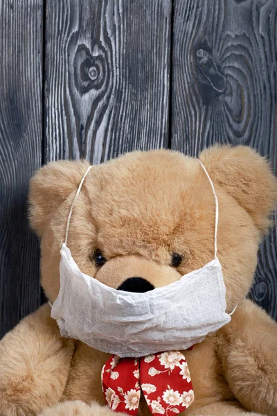 Soft toy, bear, in a protective gauze mask. Against the background of brushed boards. Protection against a viral epidemic.