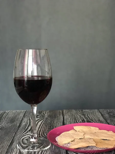 A glass of dry red wine and unleavened bread on a plate. On brushed pine boards. On a gray background. Celebration of the Lord's Supper.